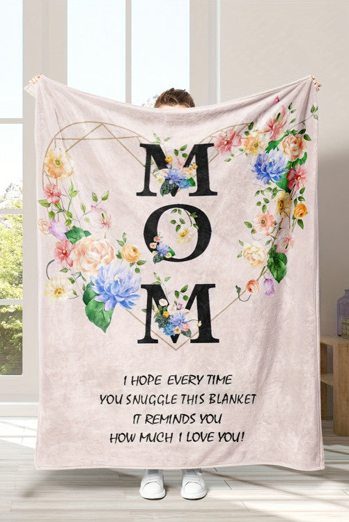Person holding a floral 'Mom' blanket with a message in a room with large windows.