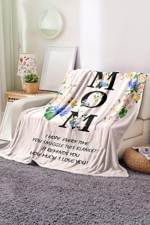 Floral 'Mom' blanket with heartfelt message on a couch in a cozy living room.